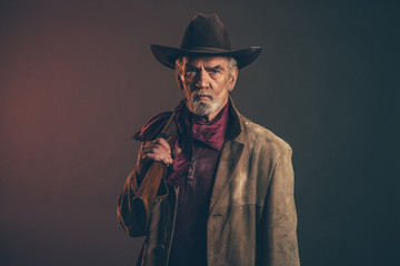 Stary szorstki zachodni kowboj z szarą brodą i brązowym kapeluszem trzyma r