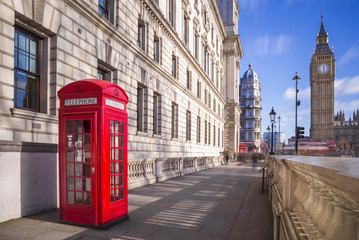 London, United Kingdom - Traditional red british telephone bopoth with Big Ben and Double Decker bus at the background on a sunny afternoon with blue sky and clouds
