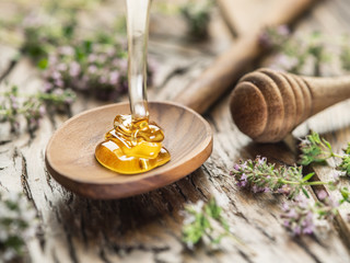 Miód ziołowy wlewamy do drewnianej łyżki. Łyżka jest na starym drewnie