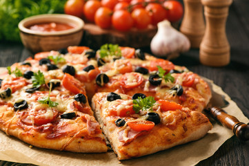 Domowa pizza z szynką, serem, pomidorami i oliwkami.