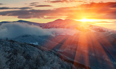 Panoramic view of winter mountains at sunrise. Landscape with foggy hills and trees covered with rime. Dramatic cloudy over sky. 