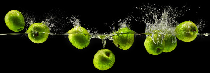 Zielone jabłko spada w wodzie na czarnym tle