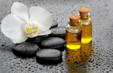 Biała orchidea i czarne kamienie, butelki z olejem.