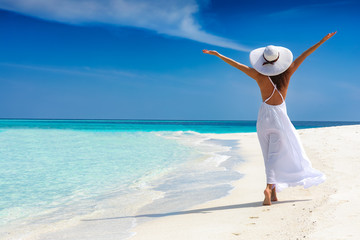 Atrakcyjna kobieta w białej sukni biegnie na tropikalnej plaży i jest szczęśliwa