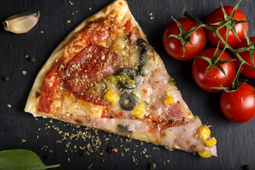 Kawałek włoskiej pizzy Capriciosa na ciemnym łupku z suszonym oregano