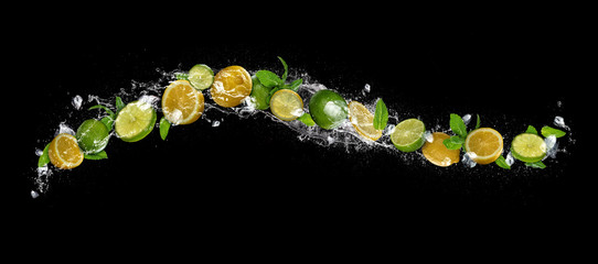 Plasterki limonki i cytryny objętych w plusk wody na czarnym tle