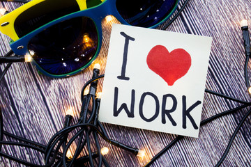 Kocham pracę Serce odręcznie na białym papierze z czarnym kolorem i kształtem serca na czerwono. Drewniane tło z 2 glasees w niektórych kolorach i ze światłami w kolejności losowej. Kocham koncepcję pracy.