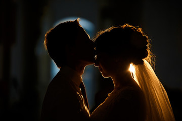 Widok z boku małżeństwa w ciemności. Pan młody całuje pannę młodą na czole, w świetle latarni. Sylwetka ślubna para