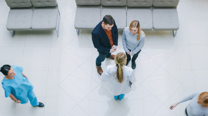 High Angle Shot in the Hospital Lobby, Young Couple Talks Meets with Female Physician / Doctor / Nurse, they have Discussion. New, Clean, Modern Hospital with Friendly and Professional Personnel.