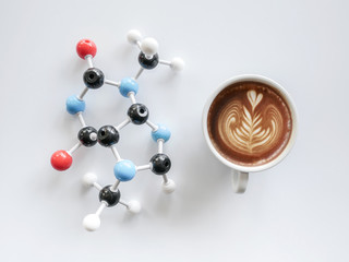 Filiżanka kawy cappuccino z latte sztuki i cząsteczki struktury kofeiny na białym stole