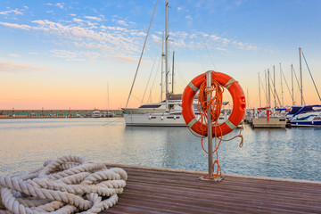 the quay of a marina at the sunset /a mooring rope with a lifebelt on the quay of a marina at the sunset