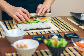 Szczegółowo ręce szefa kuchni kobieta toczenia japońskie sushi z ryżem, awokado i krewetkami na arkuszu wodorostów nori