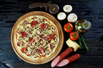 Gorąca pizza z salami, pieczarkami, pomidorami i serem na drewnianej desce. Gotowana pizza i surowi składniki na ciemnej drewnianej powierzchni.