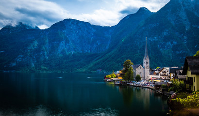 Dramatyczna sceneria wieczorna wysokich gór skalistych i miasta Hallstatt nad szerokim jeziorem