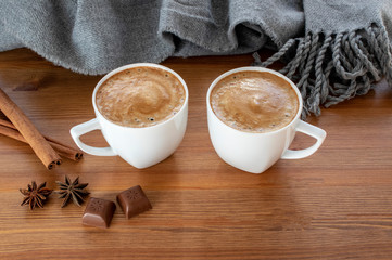 Dwie filiżanki kawy z cynamonem, anyżu i czekolady w pobliżu ciepły szalik na drewnianym stole.