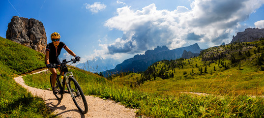 Turystyczne kolarstwo w Cortina d'Ampezzo, wspaniałe Cinque Torri i Tofana w tle. Man riding MTB enduro flow trail. Prowincja Południowego Tyrolu we Włoszech, Dolomity.
