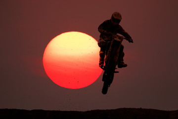 Sylwetka motocross skacze na wzgórzu z brudu paticle i dużym słońca tłem.