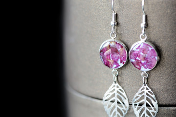 Dangle kolczyki z żywicy z płatkami róż na ciemnym tle z bliska