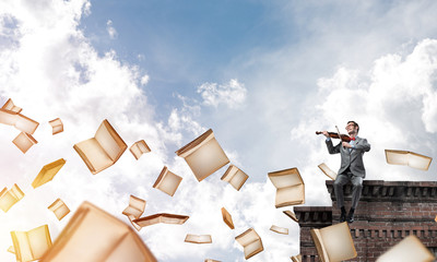 Przystojny skrzypek gra swoją melodię i latające książki