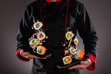 Szef kuchni trzyma talerze z latającymi kawałkami sushi.