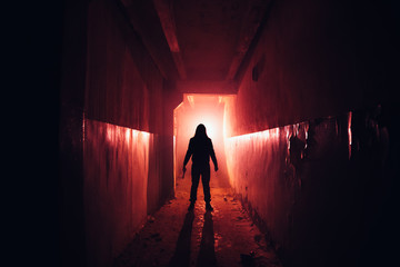 Creepy silhouette with knife in the dark red illuminated abandoned building. Horror about maniac concept