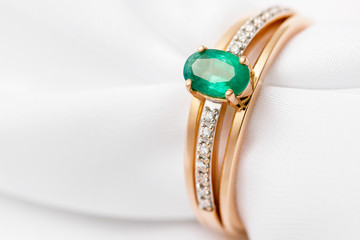 Piękny złoty pierścionek ze szmaragdowymi i sześciennymi cyrkoniami na białym jedwabiu z miejscem na kopię