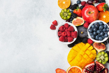 Healthy raw rainbow fruits, mango papaya strawberries oranges passion fruits berries on oval serving plate on light kitchen top, top view, copy space, selective focus