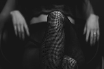 szczupła seksowna kobieta w czarnych pończochach siedzi na krześle na czarnym tle. czarny i biały