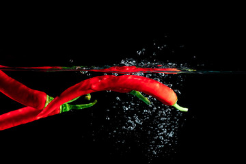 Świeże czerwone chili pod wodą na czarnym tle.