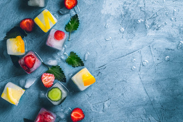 Kostki lodu z owocami i łamanym lodem na kamiennym niebieskim tle z liśćmi mięty i świeżymi owocami. Mięta, truskawka, wiśnia, cytryna, pomarańcza. Leżał płasko, widok z góry