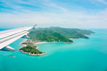 Aerial view of airplane flying above clouds and sky. Airplane wing fly over tropical green island. View from the plane window.