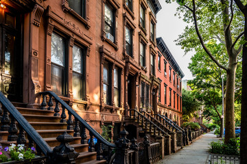Scenic view of a classic Brooklyn brownstone block with a long facade and ornate stoop balustrades on a summer day in Clinton Hills, Brooklyn