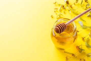Słoik płynnego miodu z kwiatów lipy i kij z miodem na żółtym tle