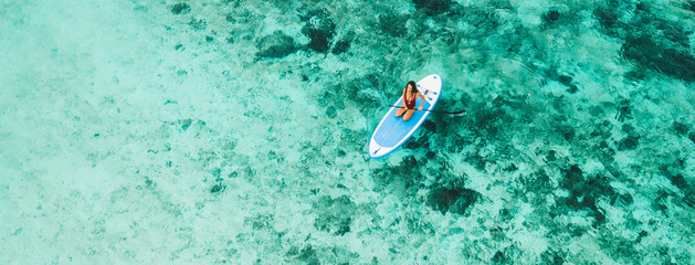 Woman sitting on sup board and enjoying turquoise transparent water and coral reef. Tropical travel, wanderlust and water activity concept.