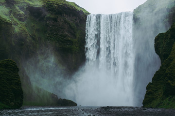 Majestic Skogarfoss waterfall in Iceland. White and green splashes flying all around against green hills covered with moss.