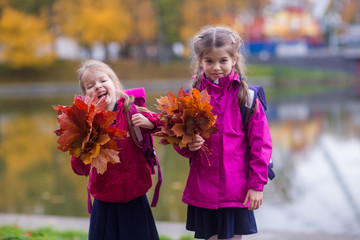two little smiling girls in school uniform with autumn leaves in park