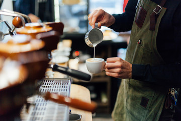 Barista making coffee in coffee shop, hands holding cup of coffee.