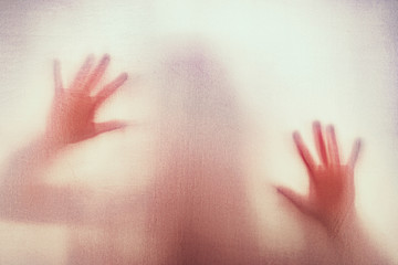 Shadow of scary paranormal ghost horror woman behind the matte red glass in soft focus. Blurry hand and body figure abstraction.
