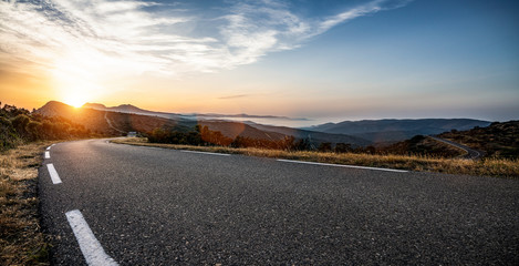 Empty long mountain road to the horizon on a sunny summer day at bright sunset