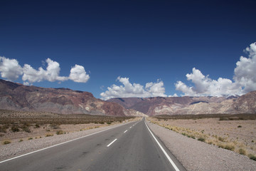 długa płaska droga asfaltowa ciągnąca sie po horyzont z górami i niebem w tle