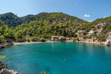 During a sunny summer day view of a beautiful small quiet cove with a pebble beach and turquoise blue water, green vegetation covered hill in the background, Mala Stiniva beach, Hvar Island, Croatia.