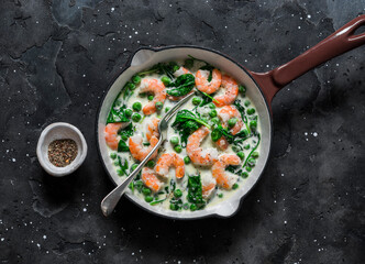 Fresh green peas, shrimps, spinach, cream sauce in a cooking pan on a dark background, top view