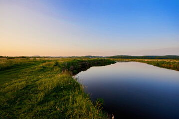 Beautiful blue Narew river flowing next to the green grass near Łomża