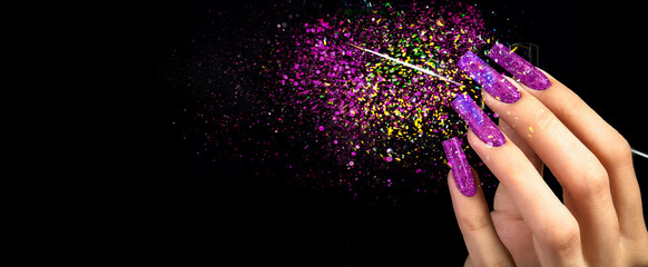 Ręka z jasnym manicure i pędzelkiem na czarnym tle usiana iskierkami. 