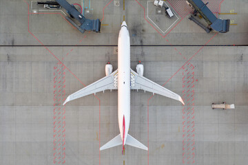 Top down view on comercial airplane docking in terminal in the parking lot of the airport apron, waiting for services maintenance, refilling fuel services after airspace lock down