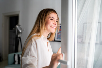 Beautiful smiling woman opening window at the morning