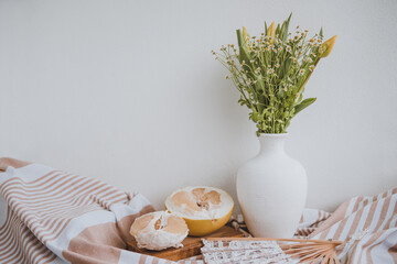 rustical still life with pomelo and fresh simple bouquet of yellow tulips and wild camomile and laced hand fan, white background, space for text
