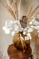  Kompozycja suszonych kwiatów i ziół w szklanym wazonie na beżowym tle ściany. 