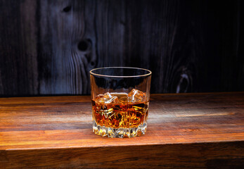 Glass of whiskey with ice cubes on an oak wooden board.
