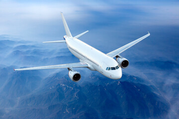 White passenger plane fly above the foggy mountain landscape. Front view of aircraft.
